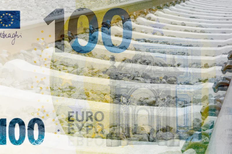 100-Euro-Schein liegt transparent über Bahngleis des ÖPNV