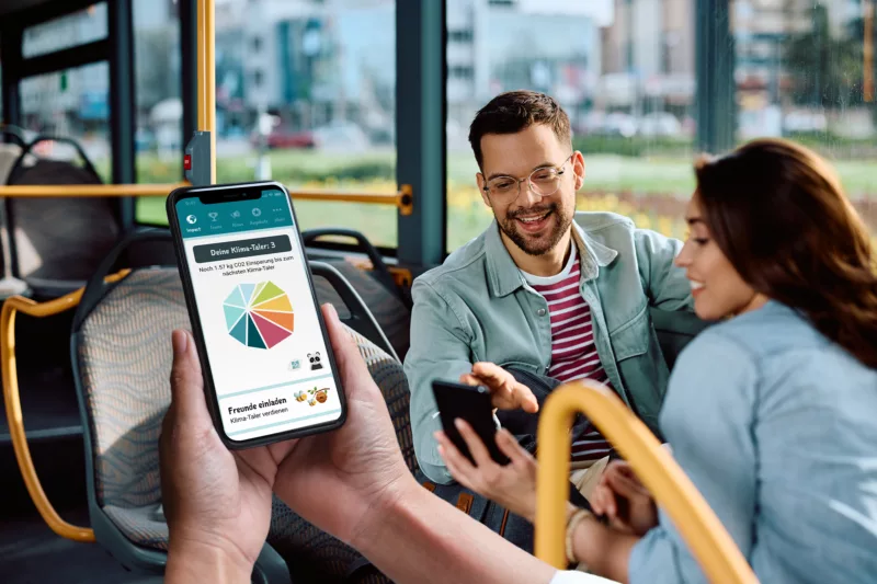 Hände halten Smartphone mit Klima-Taler-App im ÖPNV