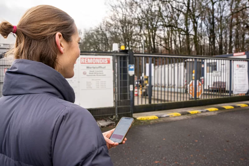 Frau mit Handy öffnet Tor zum Wertstoffhof per App